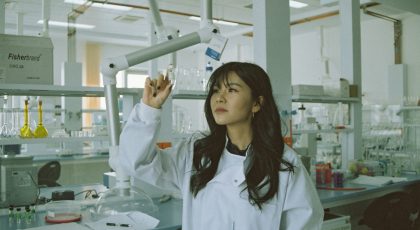 A scientist holding a lab tube up in the air, examining it.