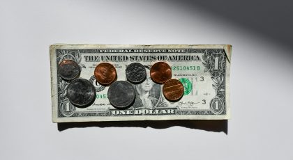 A dollar banknot with coins scattered across its surface.