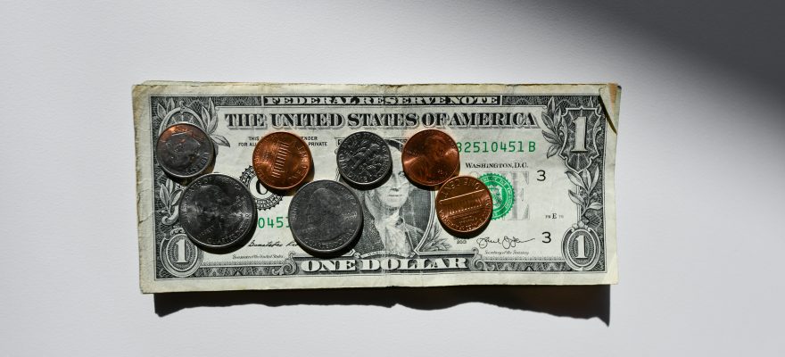 A dollar banknot with coins scattered across its surface.