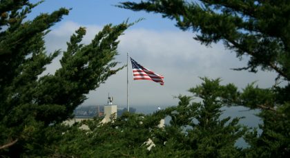 Uzaktan bir yerde Amerika bayrağı, ağaçların arasında dalgalanıyor.