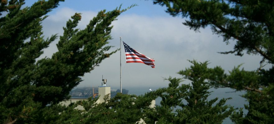 Uzaktan bir yerde Amerika bayrağı, ağaçların arasında dalgalanıyor.
